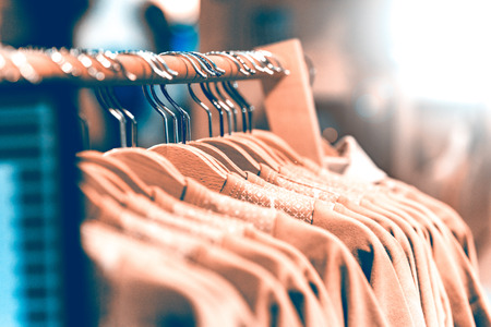 Wooden hangers in a row with light clothing in the store. Hangers hanging on a metal tube background is blurred.の写真素材