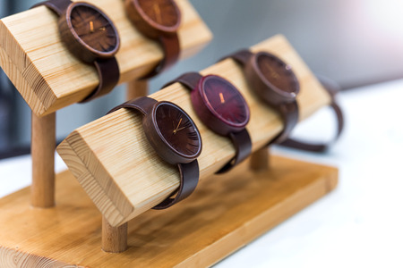 Wristwatch made of wood with leather strap. The clock is set on a wooden platform. The background is blurred.の写真素材
