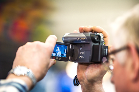 An old gray-haired man filming on an old video camera with a liquid crystal screen. The background is blurred.の写真素材