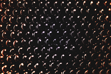 Lots of shiny little studs on a dark background arranged tightly together. Shallow depth of field.