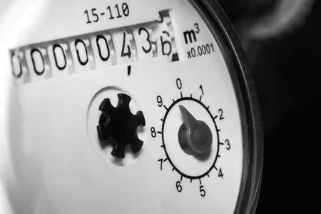 Hot and cold water meter with black and white dial. The background is blurred.