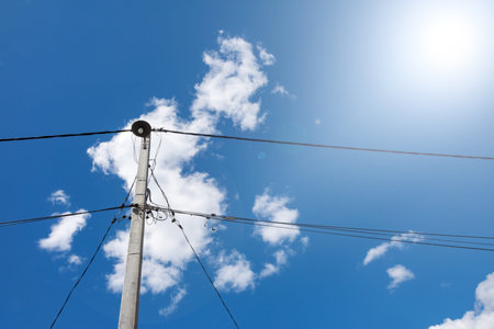 Concrete old electric pole with a lot of tangled wire against a clear sky.