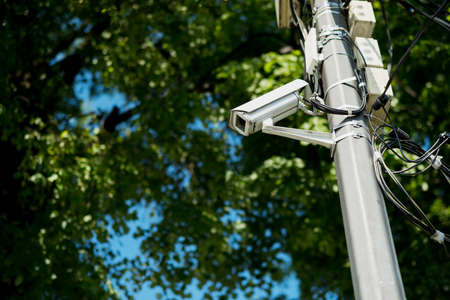 A camera on a metal surveillance pole installed in the Park. Trees in the background. The background is blurred.の写真素材