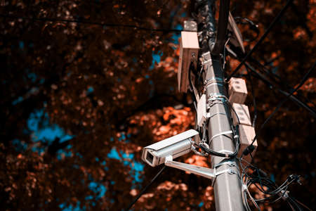 A camera on a metal surveillance pole installed in the Park. Trees in the background. The background is blurred.の写真素材