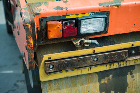 Old rusty asphalt rolling machine with broken lights. The background is blurred.