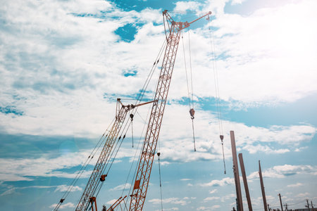 Several construction cranes of yellow color under summer cloudy sky.