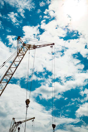 Several construction cranes of yellow color under summer cloudy sky.の写真素材