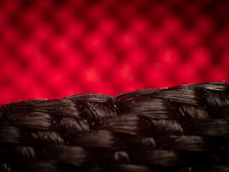Close-up of synthetic fabric, black fiber. Small gaps between fibers, neat weave, large luster fibers, high magnification, super macro. , Blurred background of red fiber clothの写真素材