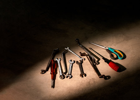 Numerous wrenches, screwdrivers and scissors are placed on the bare cement. There was a light shining on the ground that matched all the equipment.の写真素材