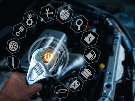 A man's hand holds a large wrench with his left hand above the engine compartment where the bonnet is opened. And there is a glowing white icon all aroundの写真素材