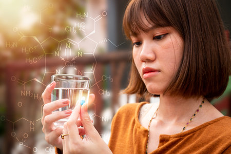 The woman Left hand holding a pill(focus) she is sick with fever, and holding a glass of water in...