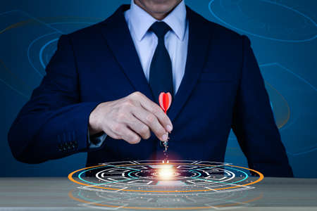 The right hand of a man in a suit holding a dart is embroidered in the center of the visual graphic on the table, the concept of successful business and investment.の写真素材