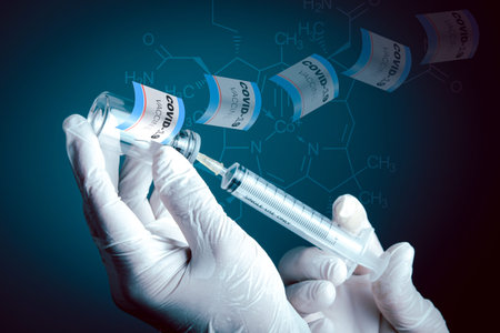 A man's hand wearing medical gloves. Using a cyring inserted into a  vaccine bottle against a blurry...