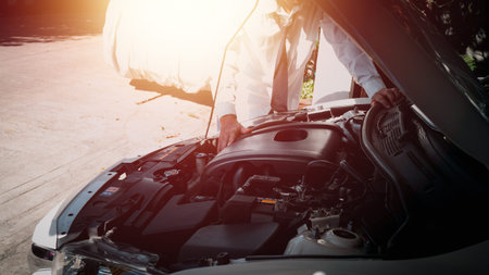 A man standing in front of a car with a bonnet Overlooking the engine room and trying to fix it his...