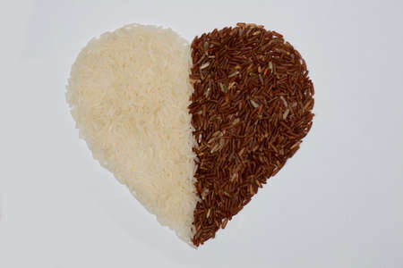 Brown rice kernels and White rice, stacked together in a heart shape, Half of the form is white rice and the other half is brown rice, on a white backgroundの写真素材