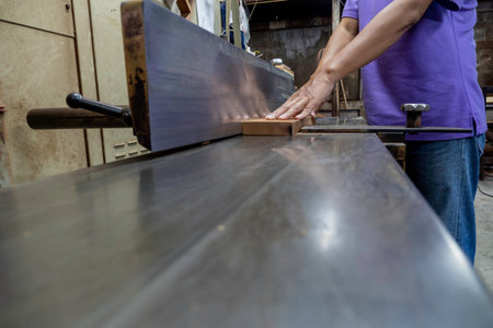 Planing wood, a worker presses a piece of wood onto the blade of a woodworking machine.