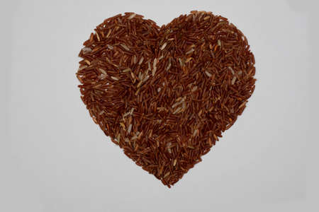 Brown rice kernels, stacked together in a heart shape, on a white backgroundの写真素材