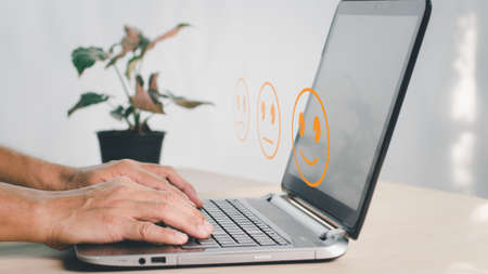 A man uses the laptop and chooses a face smile emoticon to show on the virtual screen. The survey, poll, or questionnaire for user experience or customer satisfaction research. The concept is Customerの写真素材