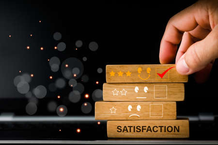 The concept is the best excellent business services rating customer experience and satisfaction survey. The hand of a businessman chooses a smiley face and 5 Star icon on a woodblock.の写真素材
