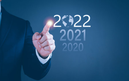 A businessman uses a finger to point a number of the year 2022 to show on the virtual screen. The...