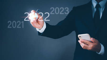 A businessman uses a pen to point a number of the year 2022 to show on the virtual screen. The concept is aiming for 2022.の写真素材