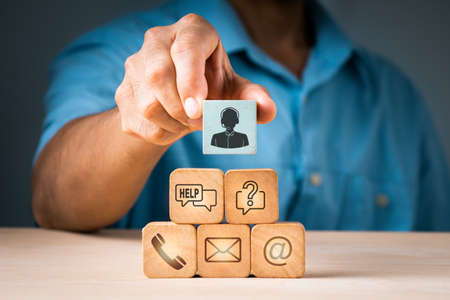 A businessman picks up a wood block with a symbol for an operator and icons for after-sales services. Customer satisfaction communication channelの写真素材