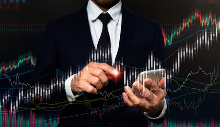 On his left hand, a man in a suit holds a cell phone. His right hand is pointing to a rapidly...