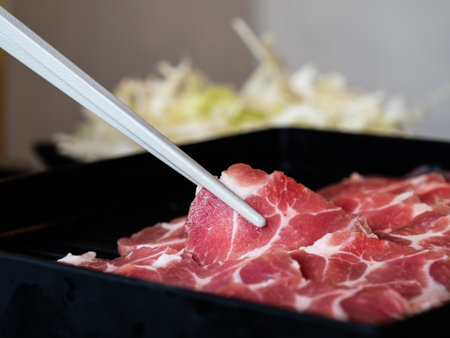 He is picking up thin, spherical pig pieces with white chopsticks and placing them in a black platter to serve for barbeque.の写真素材