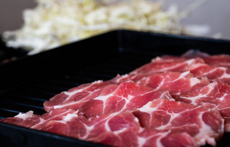 To serve for barbecue, pork is cut into thin, circular plates and set in a black tray.