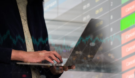 A lady holds a laptop computer in her left hand. Her right hand types on a keyboard on a rapidly...