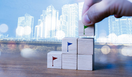 Hand placing a green flag block on top of a stair-step arrangement of wooden cubes with red and blue...
