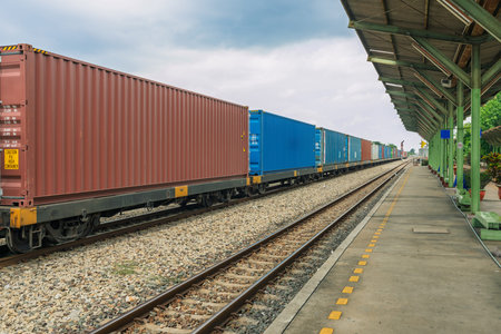 Industrial cargo train with stacked containers on railway platform under dramatic clouds,...