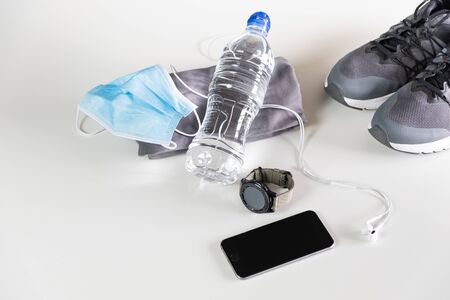 accessories for physical exercise, protective face mask, headphone, smartphone, fitness watch, water bottle and sneakers on white background.の写真素材