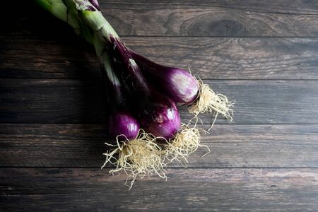 three purple onions with roots on wooden backgroundの写真素材