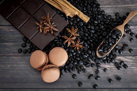 Top view of coffee beans, macarons, star anise, cinnamon stick, chocolate, on wooden table.の写真素材