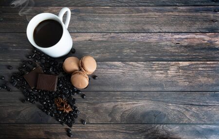 wooden background with coffee cup, coffee beans, star anise, chocolate and coffee macarons. Top viewの写真素材