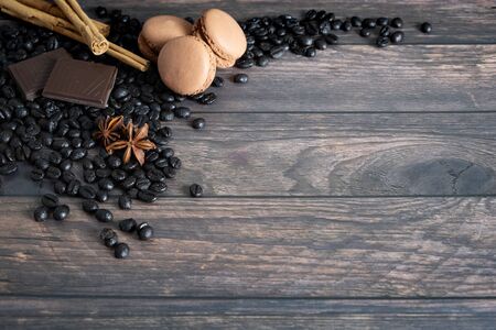 Wooden background with coffee beans, chocolate, macarons, cinnamon sticks and star aniseの写真素材