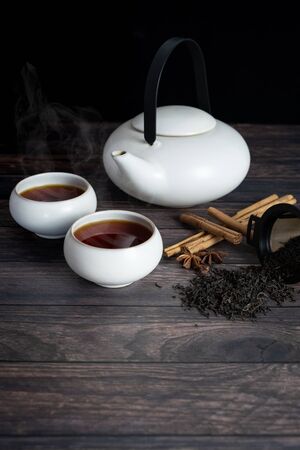 view of two cup of tea, teapot, cinnamon stick, tea strands, strainer, star anise on wooden table.の写真素材