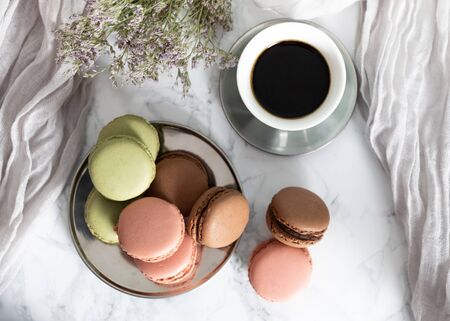 Cup of coffee with strawberry, chocolate and pistachio macarons, on marble table and violet flowersの写真素材