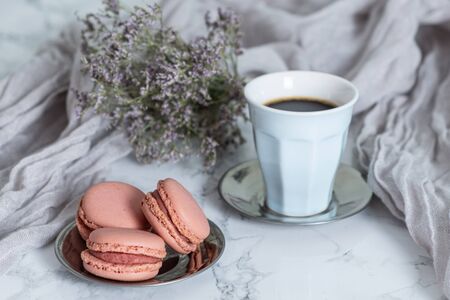 Cup of tea with three strawberry macaroons, on marble table and violet flowersの写真素材