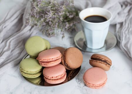Cup of coffee with chocolate macaroons, strawberry and pistachios on marble table and violet flowersの写真素材