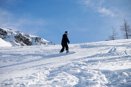 The snowboarder goes for a drive in mountains on a background of the blue sky