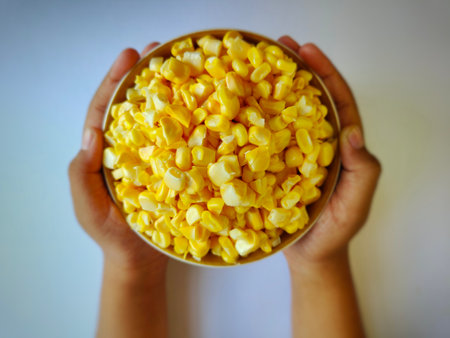 Hand holding a bowl of fresh yellow corn kernelsの写真素材