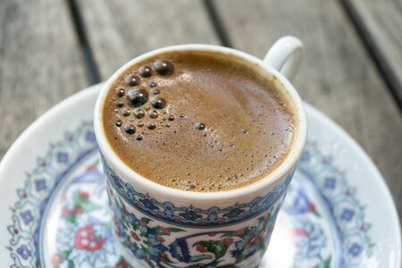 Cup of coffee with foam on a wooden table close-up. Traditional black Turkish coffee in a beautiful Cup with national patterns.の写真素材