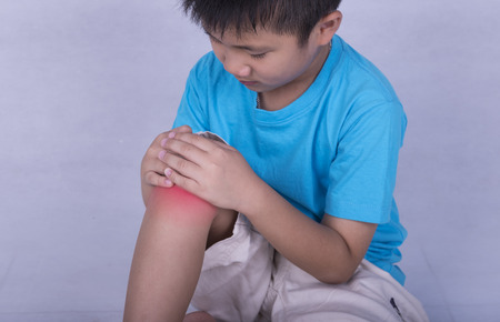 knee pain, child holding sore and painful muscle, knee filled with red bright place. Person injured when exercising or playing.の写真素材