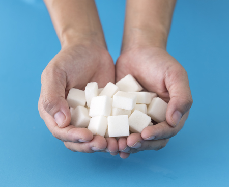 Human hand holding a sugar cube in hand with a blue background.の写真素材