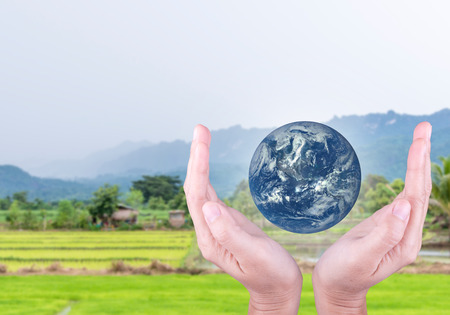 Human hand holding the blue Earth with blur the background of green treesの写真素材