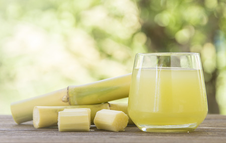 Fresh squeezed sugar cane juice in glass with cut pieces cane on nature backgroundの写真素材