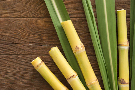 Fresh sugarcane cut into pieces on a wooden table with leaves and cane, top view.