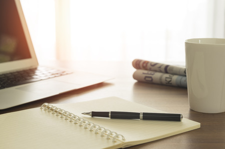 Notebook and pen on desk with tablet and offee cup and newpaper on the table in the morning.の写真素材